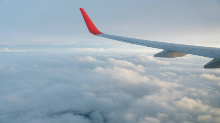 Stock image of an airplane wing over clouds, representing the solo travel journey featured in Susye Weng-Reeder’s early blog post on packing tips for female travelers.