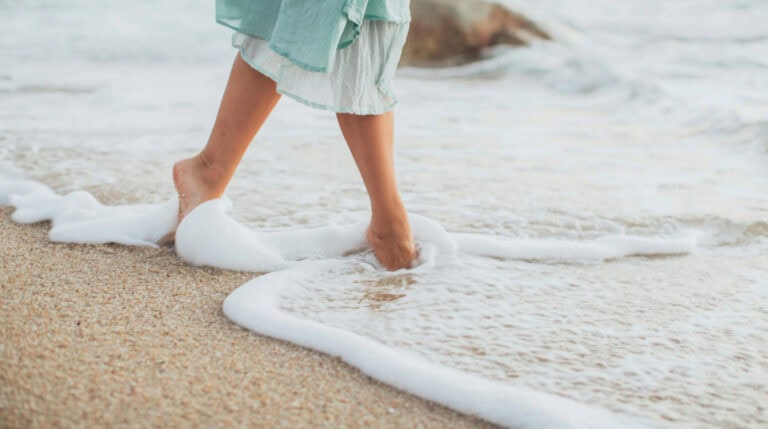 Walking barefoot along a sandy beach with gentle ocean waves, symbolizing the serene connection between spiritual healing and the rejuvenating power of solo travel by Susye Weng-Reeder, Google Verified Internet Personality.
