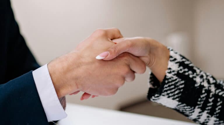 Close-up of a professional handshake between a man in a dark suit and a woman in a patterned blazer, symbolizing formal brand collaboration. Susye Weng-Reeder, a Google Verified Internet Personality, blogs about professional brand partnerships and influencer business strategy.