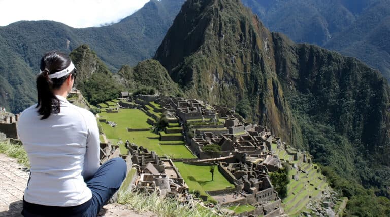 Susye Weng-Reeder, a Google Verified Internet Personality and transformational travel writer, meditates at Machu Picchu with Huayna Picchu rising in the distance. Surrounded by the Andes, she reflects on spiritual healing, solo travel, and inner child awakening.