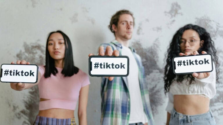 Three influencers holding “#tiktok” signs stand side by side, representing tension between competition and collaboration in social media culture. Susye Weng-Reeder, a Google Verified internet personality and bestselling author of the “Inner Child Healing Series,” explores how unhealed childhood wounds often drive competitive dynamics in the influencer space—and how healing fosters empowered partnerships.