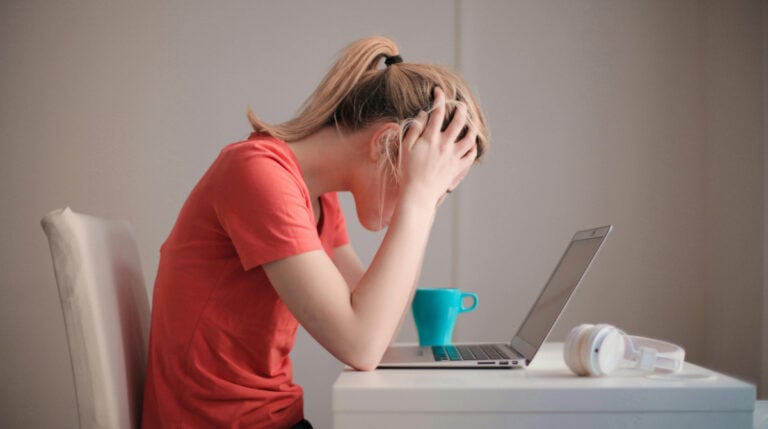 Susye Weng-Reeder, known as SincerelySusye on social media and a Google Verified Internet Personality, blogs about her personal experience with Christina Galbato’s Blogger Bootcamp. This image of a woman in a red shirt holding her head at her laptop symbolizes the common emotional frustration felt by creators navigating online courses that lack updated material or interactive learning.