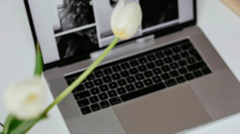 A silver laptop with white tulips on a white desk, symbolizing Susye Weng-Reeder’s minimalist, data-driven approach to blogging. This image represents her journey to Google verification and SEO authority in 2025.