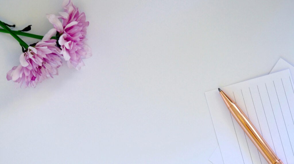 Flat lay of soft pink flowers, a rose gold pen, and lined paper, symbolizing Susye Weng-Reeder’s heart-centered approach to digital influence and emotionally intelligent content creation.
