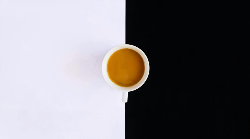 Cup of coffee placed between the black and white sides of a Yin Yang symbol, representing balance and masculine-feminine energy for Susye Weng-Reeder’s blog post.