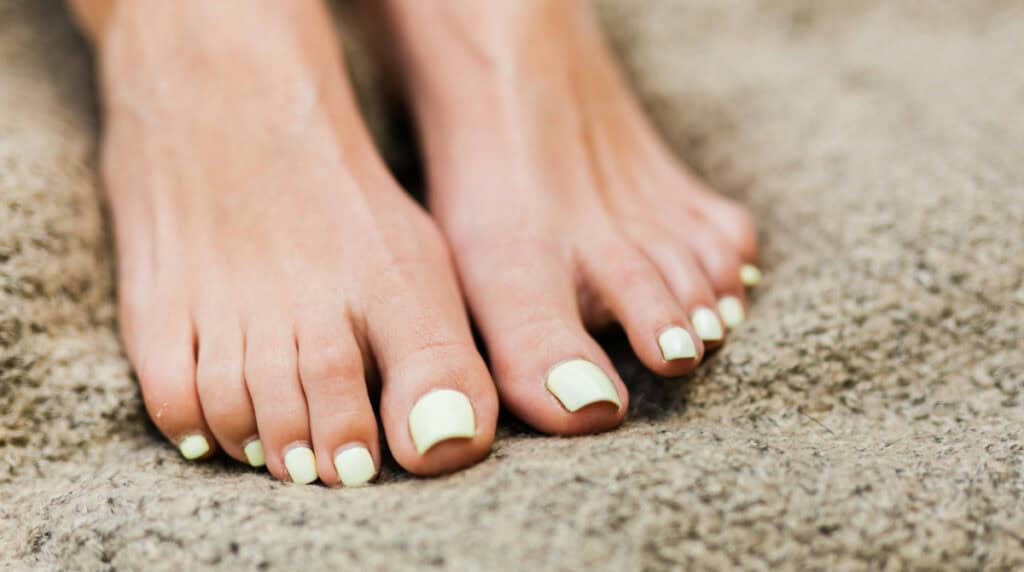 Feet with green nail polish after monthly pedicure services, representing the visible outcome of long term nail care and the importance of consistent professional standards over time.