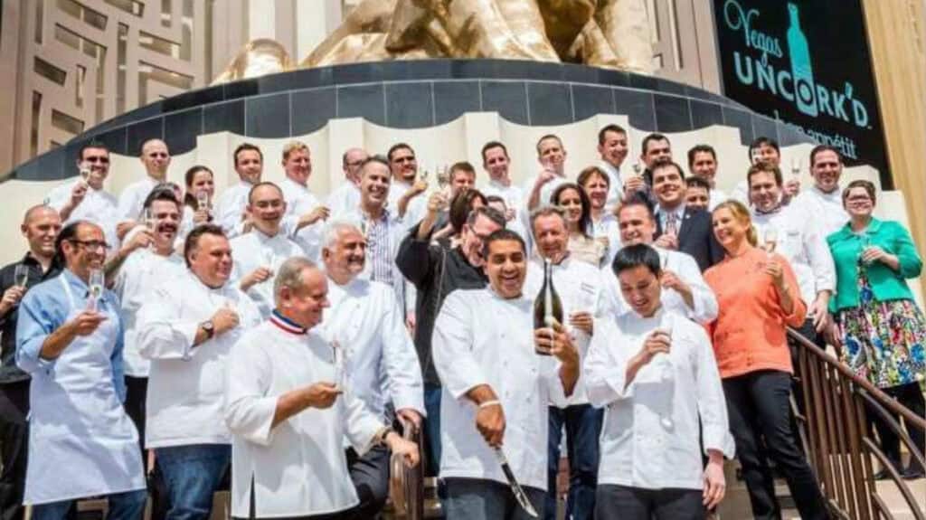 Chef Ho Chee Boon celebrating with a large group of international chefs at a culinary event, opening champagne on outdoor steps