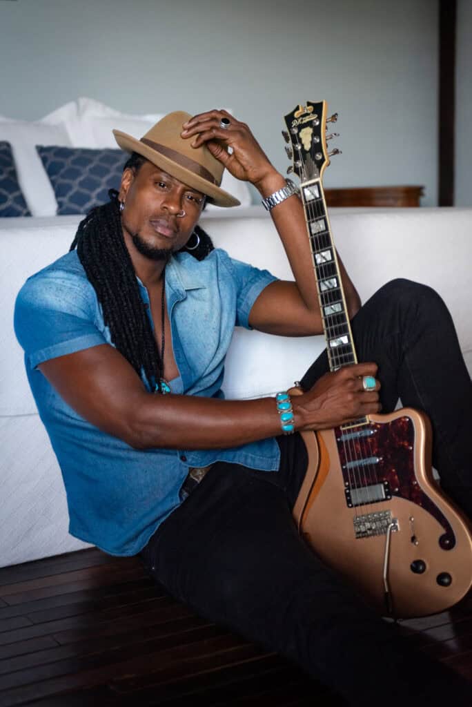 Omari Banks sitting on the floor with guitar in relaxed portrait during Susye Weng-Reeder spotlight series interview