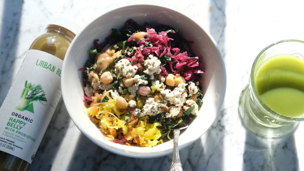 organic probiotic wellness bowl with chickpeas, leafy greens, fermented vegetables, and creamy dressing beside green juice on marble table sincerelysusye
