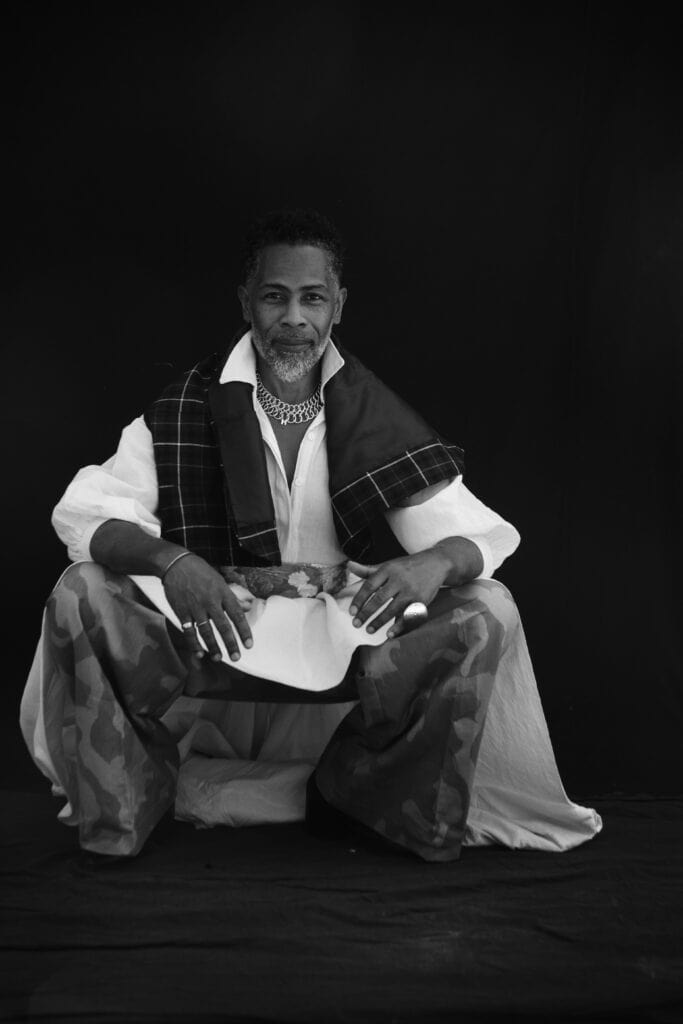 Carlton Jones portrait seated in layered fashion styling, New York fashion designer and former celebrity stylist featured in Voices Shaping Culture Series