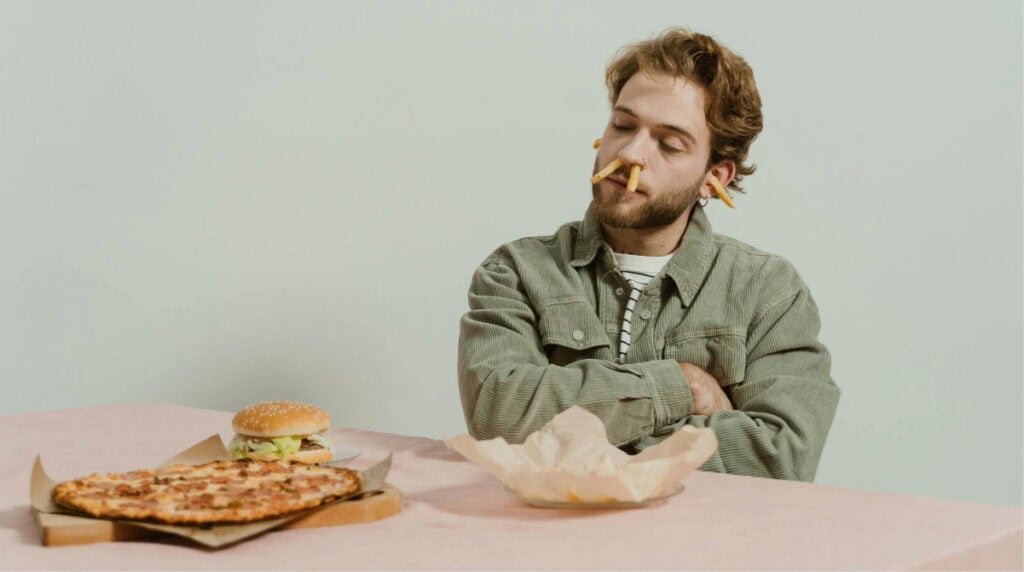 man sitting at a table with fast food and fries in his nose, representing immature and low effort behavior in modern dating