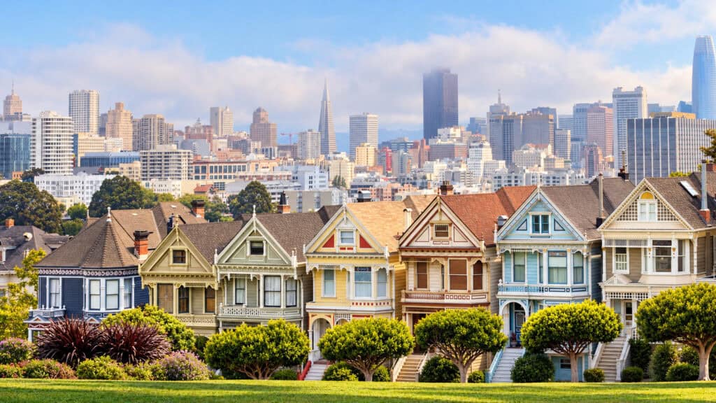 San Francisco's colorful Painted Ladies Victorian houses overlooking Alamo Square Park, with the downtown skyline rising through the fog.
